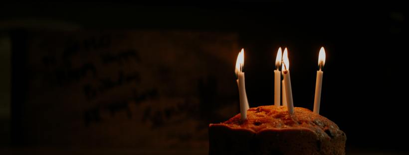 A simple birthday cake with five candles in the dark, on a table.