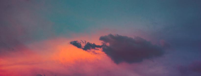 A dawn sky with hues of blue, pink, orange behind clouds